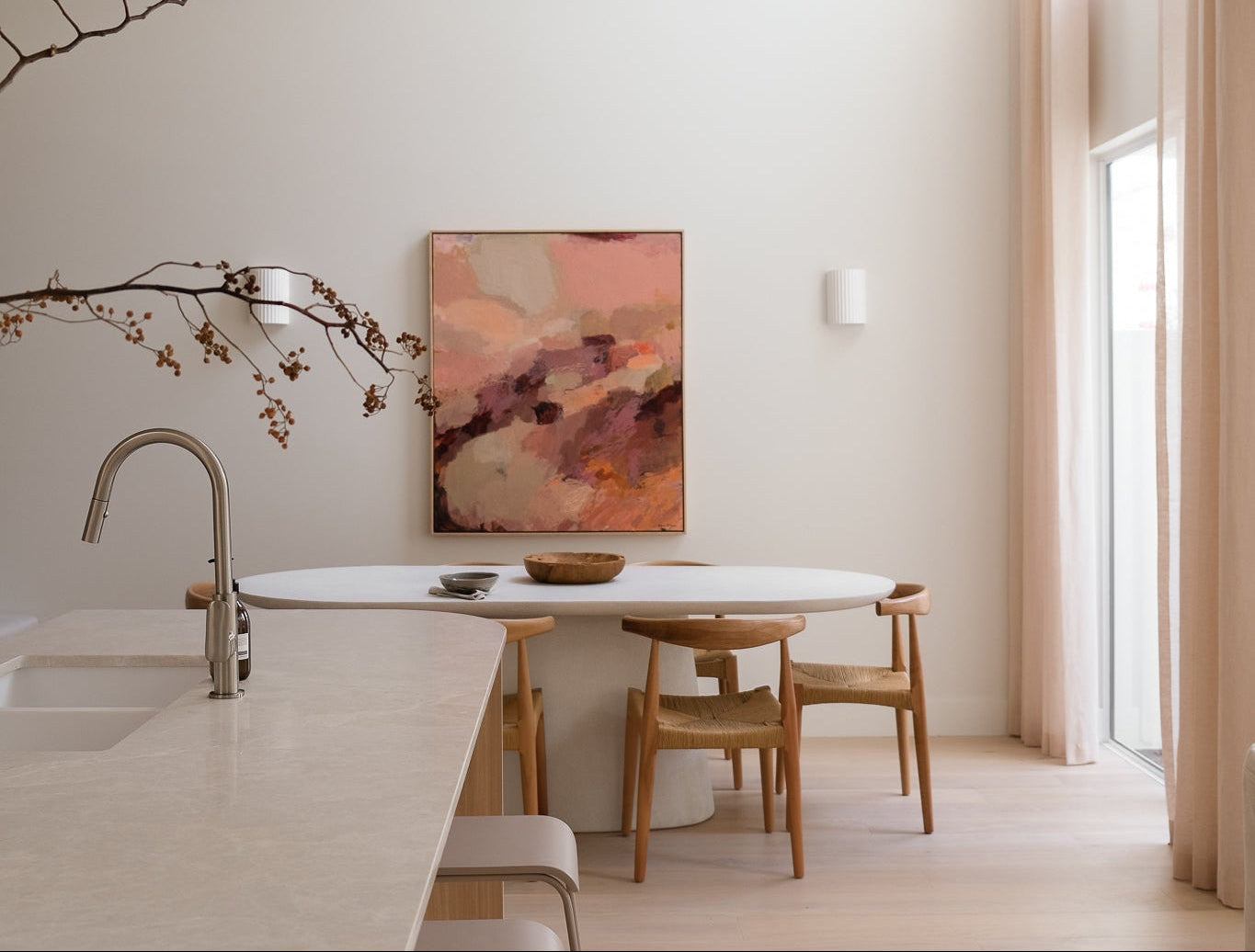 Modern kitchen with marble island, wooden chairs, and abstract art on the wall.