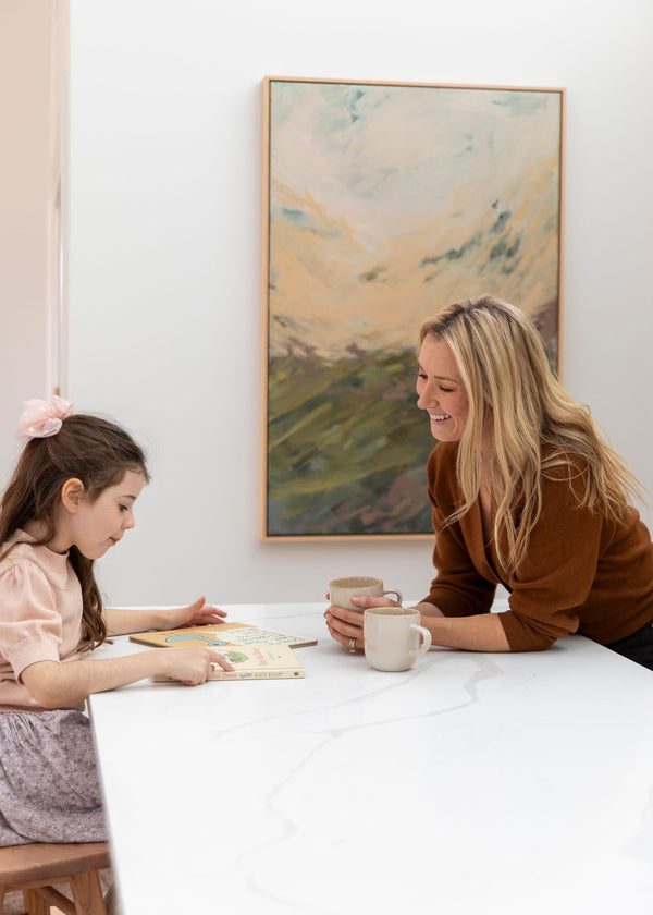 Woman and child sitting at a table with a book, smiling in a home setting.