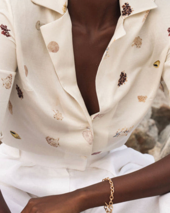 Close-up of a person wearing a white floral blouse with a brown top underneath, sitting on a stone surface.
