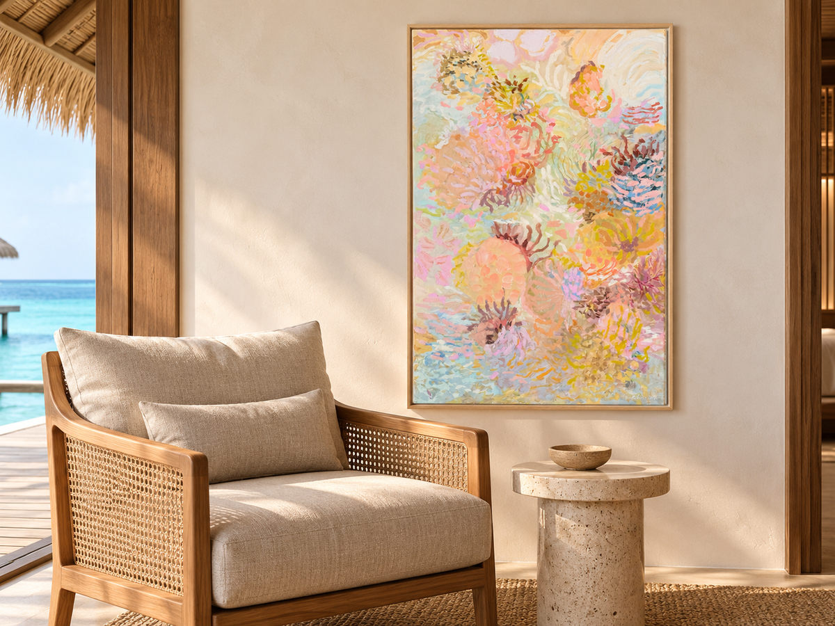 Coral Wanderings by Prudence De Marchi displayed beside a timber and woven armchair in a coastal interior.